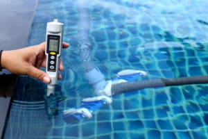 Aspirador de Limpeza de piscina na água e uma pessoa segurando um aparelho eletrônico de medição do cloro