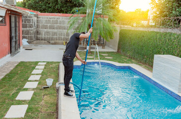 Rapaz fazendo uma Limpeza de piscina com um aspirador e um cabo telescópico.